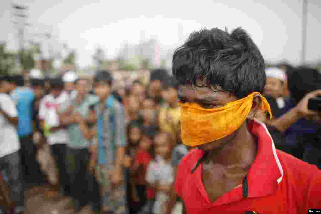 A boy covers his nose with a cloth as people gather in front of mass graves during the burial of unidentified garment workers, who died in the collapse of the Rana Plaza building in Savar, Bangladesh, May 1, 2013.