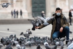 Un hombre con máscara protectora alimenta a las palomas en una plaza de Milán, Italia, el 25 de febrero de 2020.