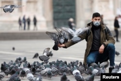 A man in a face mask feeds pigeons in Milan, as the country is hit by the coronavirus outbreak, Italy February 25, 2020. REUTERS/Yara Nardi