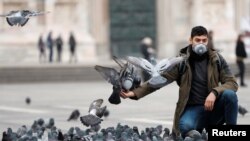 Un hombre con máscara protectora alimenta a las palomas en una plaza de Milán, Italia, mientras Europa es considerada ahora la zona más caliente del brote de coronavirus. 