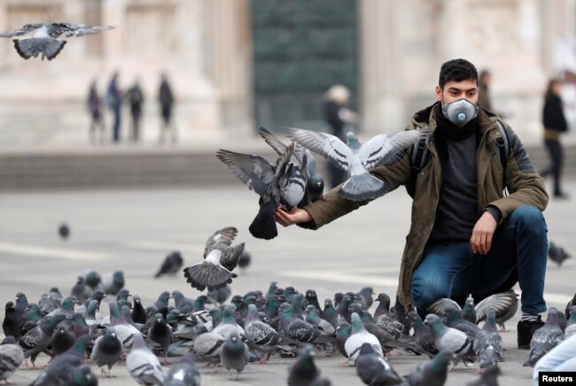 Un hombre con máscara protectora alimenta a las palomas en una plaza de Milán, Italia, el 25 de febrero de 2020.