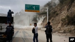 People watch as earth, dust spill on the Pan-American highway as result of an earthquake, north of Quito, Ecuador, Aug. 12, 2014.