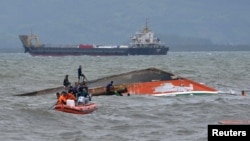 Rescuers tie a rope at the capsized vessel MBCA Kim-Nirvana to pull it towards the shore near a port in Ormoc city, central Philippines, July 3, 2015. 