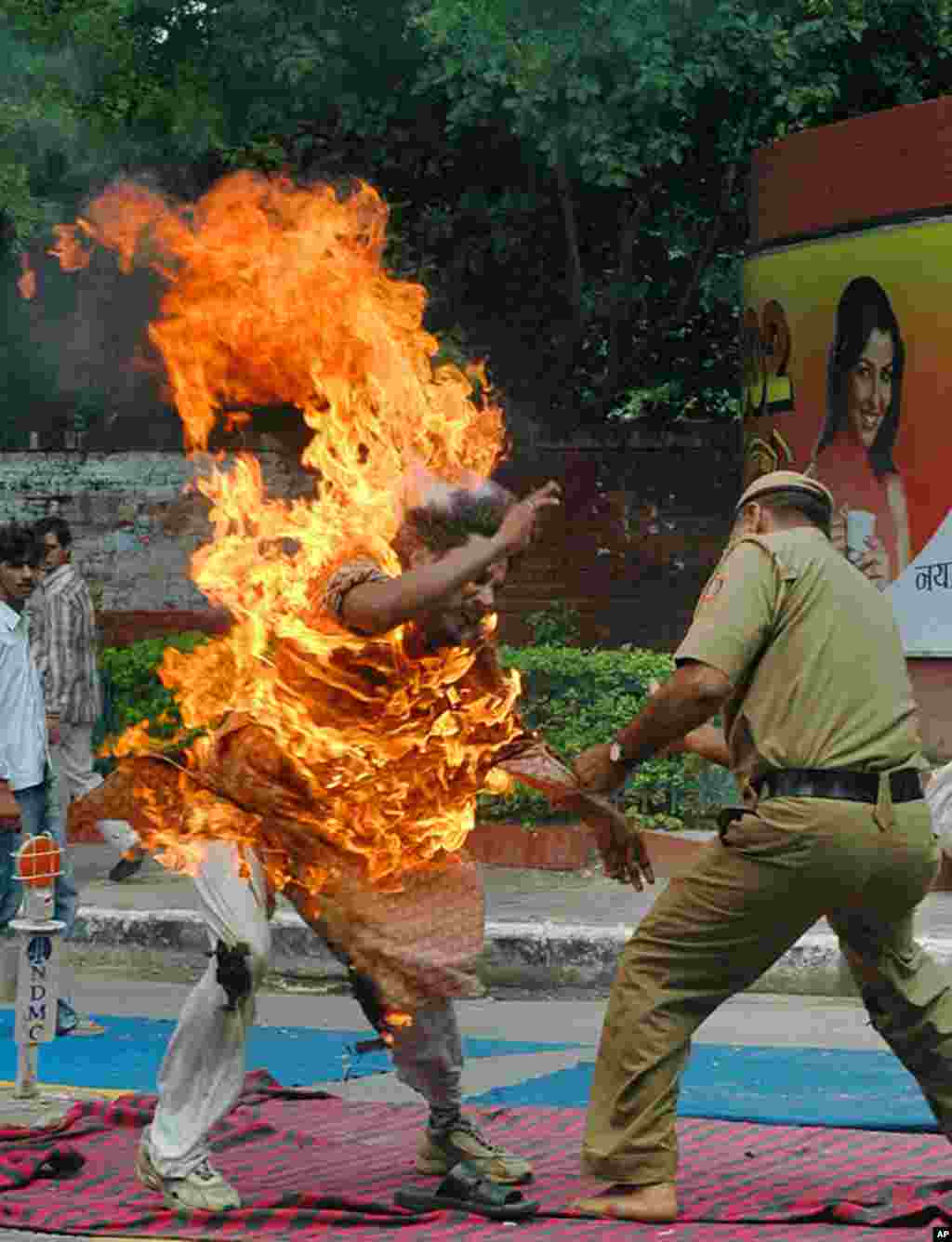 A police officer tries to douse the flames off Rajneesh Kumar, who tried to immolate himself in an act of protest in New Delhi, India. Kumar has been sitting in protest since May 25, 2006, to appeal for help in the release of his wife and three children w