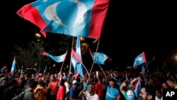 Opposition party supporters cheer and wave their party flags after Mahathir Mohamad claims the opposition party wins the General Election, broadcast on a large screen at a field in Kuala Lumpur, Malaysia, May 9, 2018.