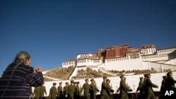 A woman prays as a group of Chinese soldiers march in front of the Potala Palace in Lhasa