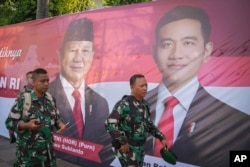 Tentara berjalan di depan spanduk yang memperlihatkan Presiden terpilih Prabowo Subianto, kiri, dan Wakil Presiden terpilih Gibran Rakabuming Raka, yang juga merupakan putra sulung Presiden Joko Widodo, di Jakarta, 20 Oktober 2024. (Foto: AP)