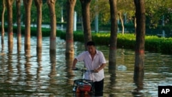 A man pushes a scooter through floodwaters in Xinxiang in central China's Henan Province, July 26, 2021. 