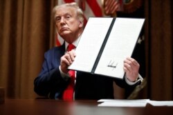 President Donald Trump holds up a signed Executive Order on hiring American workers, during a meeting with U.S. tech workers, in the Cabinet Room of the White House, Aug. 3, 2020, in Washington.