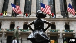រូបឯកសារ៖ មនុស្សម្នា​ដើរ​កាត់​អគារ​ទីផ្សារ​ភាគហ៊ុន​ញូវយ៉ក (NYSE) និង​រូបសំណាក ក្មេងស្រីអង់អាច 'Fearless Girl' នៅ Wall Street ថ្ងៃទី៣០ ខែវិច្ឆិកា ឆ្នាំ២០២០។ 