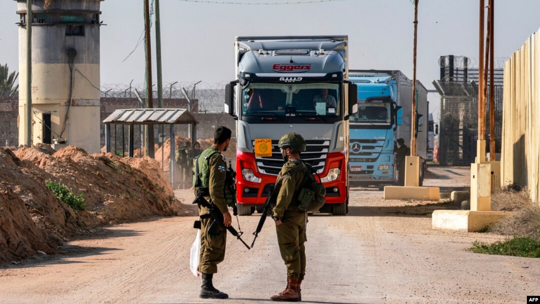 Soldados israelíes hacen guardia mientras camiones con ayuda humanitaria se aproximan. Toma captada en el lado israelí del cruce fronterizo de Kerem Shalom con el sur de la Franja de Gaza el 19 de diciembre de 2023.