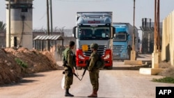 Israeli soldiers stand guard as trucks carrying humanitarian aid move at the Israeli side of the Kerem Shalom border crossing with the southern Gaza Strip on December 19, 2023, amid the ongoing conflict between Israel and the Palestinian militant group Ha