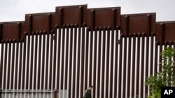 Petugas pengamanan perbatasan berjalan di sepanjang tembok perbatasan antara Tijuana, di Meksiko, dan San Diego di Amerika Serikat, 18 Maret 2020. (Foto: AP Photo/Gregory Bull)