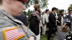 A U.S. soldier looks on as Afghan villagers, some of whom testified earlier in the week, speak through an interpreter with reporters, following a sentencing hearing for Staff Sgt. Robert Bales at Joint Base Lewis-McChord, Washington, Aug. 23, 2013.