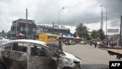 A police officer gestures next to a burnt out car that was set on fire during protests against a third term for Ivorian President Alassane Ouattara, in Abidjan, Oct. 19, 2020, ahead of presidential elections set for Oct. 31, 2020. 