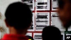 FILE - Migrants seeking asylum in the United States check their names on a printed list that's posted on a board near the international bridge, April 30, 2019, in Matamoros, Mexico.