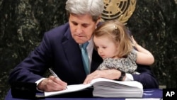 FILE - Then-U.S. Secretary of State John Kerry holds his granddaughter Isabel Dobbs-Higginson as he signs the Paris Agreement on climate change, April 22, 2016 at U.N. headquarters. 