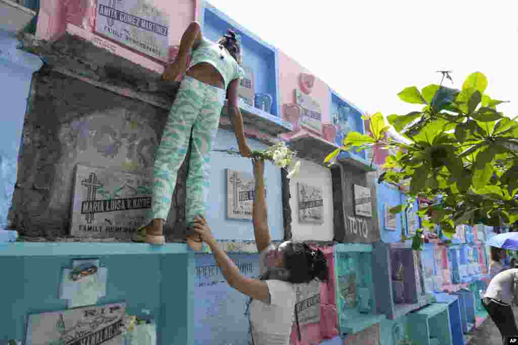 A woman hands over a flower to her daughter as she climbs to reach the tomb of their loved one at Manila's North Cemetery, Philippines, as the nation observes All Saints Day.