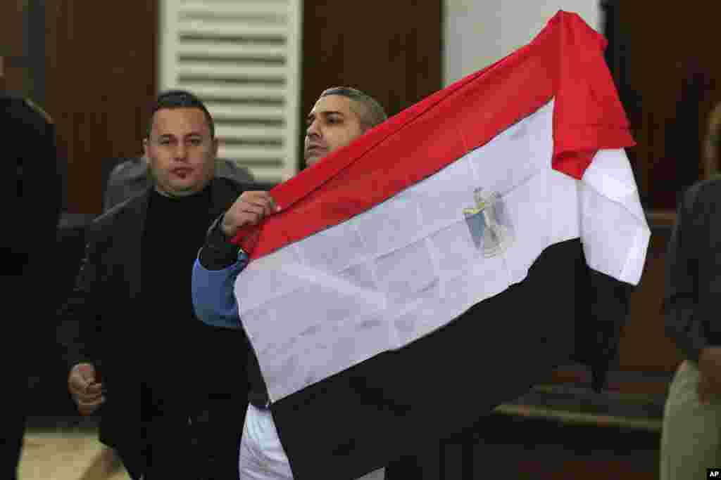 Mohamed Fahmy, a Canadian journalist of Al Jazeera English, holds up an Egyptian flag after a retrial at a courthouse near Tora prison in Cairo, Egypt. An Egyptian judge ordered Fahmy and another Al Jazeera English journalist, Baher Mohammed, released on bail as their retrial on terror-related charges continues.