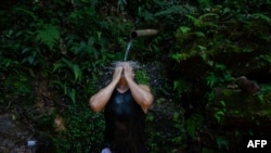 Seorang warga dari area pemukiman miskin Rocinha mendingingkan dirinya dengan air dari sumber mata air alami di lokasi tersebut di tengah gelombang panas yang melanda Rio de Janeiro, Brazil, pada 17 November 2023. (Foto: AFP/Tercio Teixeira)