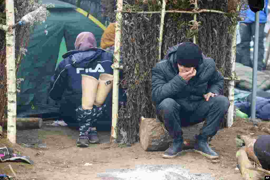 A man sits outside a tent as other migrants gather at the Belarus-Poland border near Grodno, Belarus. About 15,000 Polish troops have joined riot police and guards at the border. The Belarusian Defense Ministry accused Poland of an &quot;unprecedented&quot; military buildup there, saying that migration control did not require such a force.&nbsp;