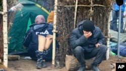 A man sits outside a tent as other migrants gather at the Belarus-Poland border near Grodno, Belarus. About 15,000 Polish troops have joined riot police and guards at the border. The Belarusian Defense Ministry accused Poland of an "unprecedented" military buildup there, saying that migration control didn't warrant such a force. 