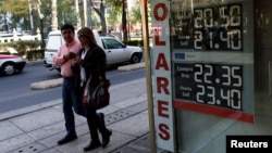 People walk pass a board displaying the exchange rate of Mexican peso against the U.S. dollar in Mexico City, Jan. 11, 2017.