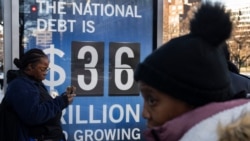 People wait for a bus near a National Debt Clock billboard display showing the United States gross national debt and each American family's share of the debt in Washington, DC, on December 30, 2024.