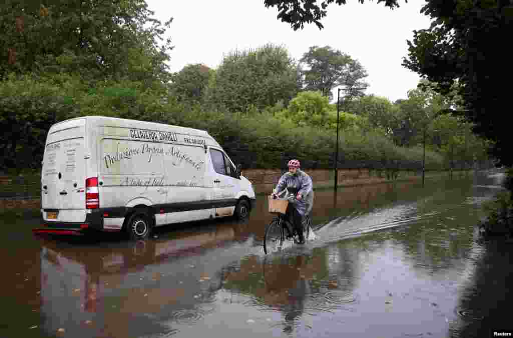 A person cycles through floodwater as heavy rain combines with water spilling over the river bank of the tidal River Thames on a road in west London, Britain.