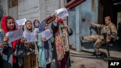 FILE - A Taliban fighter watches as Afghan women hold placards during a demonstration demanding better rights for women in front of the former Ministry of Women Affairs in Kabul, Sept. 19, 2021.