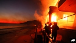 Sejumlah petugas pemadam kebakaran bekerja dari dek ketika Kebakaran Palisades melalap sejumlah properti yang ada di pinggir pantai, 8 Januari 2025 di Malibu, California. (Foto: Etienne Laurent/AP Photo)