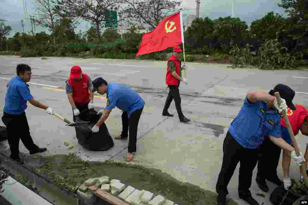 2018年9月17日，中国广东省珠海，台风山竹过后，志愿者和警察清理高速公路上的碎片，一名男子手持中国共产党的旗帜，警示过往车辆。台风山竹造成海水倒灌，樹木倒伏，但据说抗灾清理工作比较迅速。