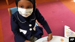 In this, May 2, 2017 photo, Amira Hassan plays in the waiting room at the specialty clinic at Children's Minnesota in Minneapolis. Hassan went to the hospital's clinic for a routine wellness check, but had to wear a mask to protect her from measles after an outbreak has sickened more than 30 children in Minnesota. 