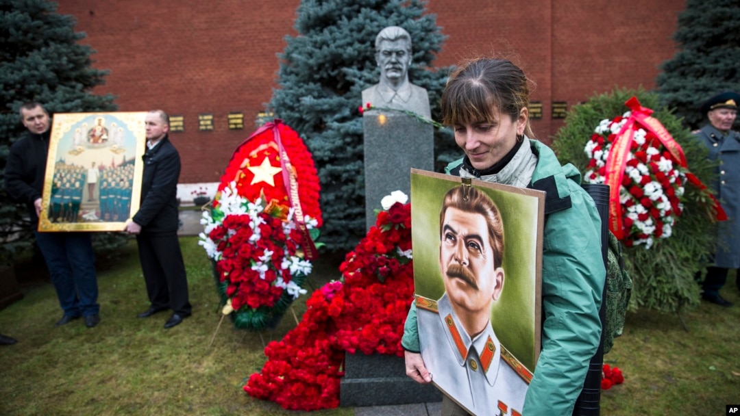 A woman holds a portrait of Joseph Stalin near the former Soviet leader's tomb near the Kremlin wall, as she came to mark the 136th anniversary of his birth, in Moscow, Russia, Dec. 21, 2015. 