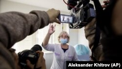 A Russian medical worker, center, shows a vial with Russia's Sputnik V coronavirus vaccine to the media prior to a shot in a hospital in Vladivostok, Russia, on Tuesday, Dec. 15, 2020. (AP Photo/Aleksander Khitrov )