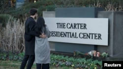 Sepasang suami istri berdiri di depan papan nama The Carter Presidential Center, setelah meninggalnya mantan Presiden Amerika Serikat Jimmy Carter pada usia 100 tahun, di Atlanta, Georgia, AS, 29 Desember 2024. (Elijah Nouvelage/REUTERS)