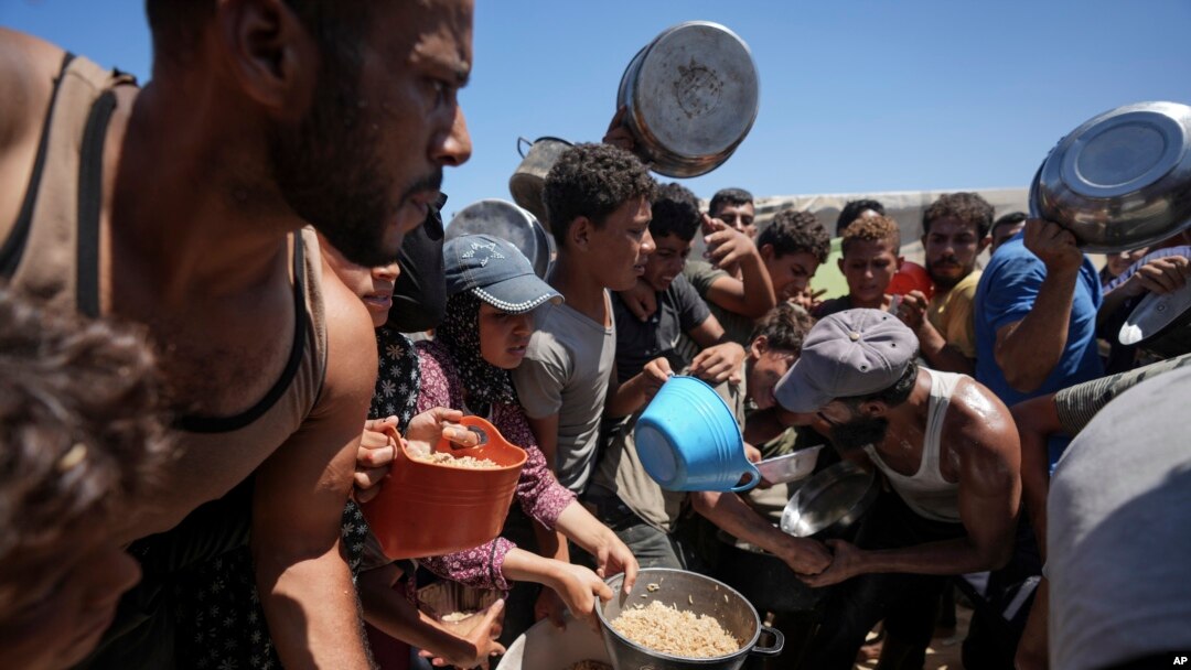 Palestinianos deslocados reúnem-se para distribuição de alimentos em Deir al Balah, no centro da Faixa de Gaza, a 23 de agosto de 2024.
