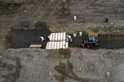 Workers wearing personal protective equipment bury bodies in a trench on Hart Island, in the Bronx borough of New York, April 9, 2020.