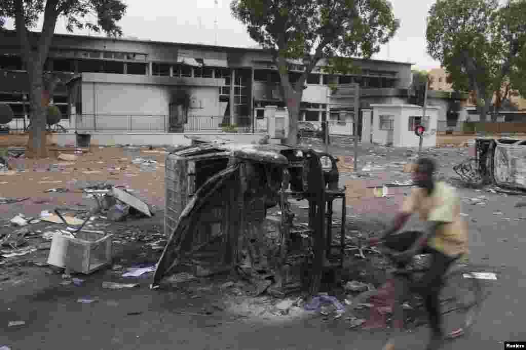 Un homme roule en bicyclette devant un amas de débris laissé après les saccages et pillages qui ont lieu jeudi 30 octobre et vendredi 31octobre 2014 lors des manifestations qui ont conduit au départ du président Blaise Compaoré du pouvoir après 27 ans de règne. 