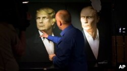 A journalist points at a portrait of U.S. President-elect Donald Trump, with a portrait of Russian President Vladimir Putin at right, during a live telecast of the U.S. presidential election in the Union Jack pub in Moscow, Russia, Nov. 9, 2016. 