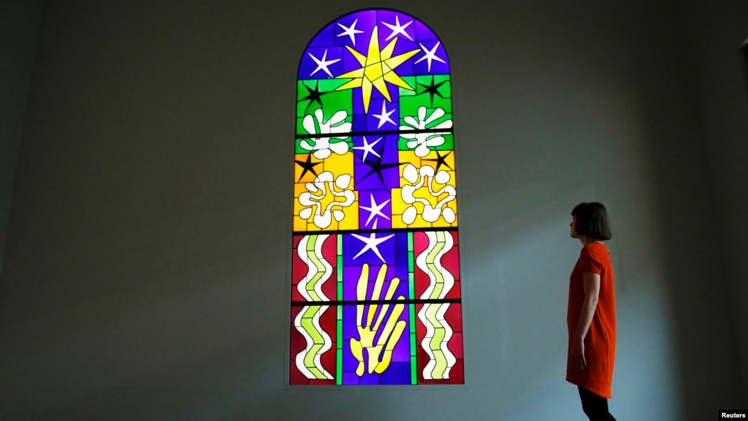An employee poses with a stained glass "Christmas Eve" (Nuit de Noel), part of an exhibition of paper cut outs - "Henri Matisse: The Cut-Outs" - at the Tate Modern gallery in London, April 2014.