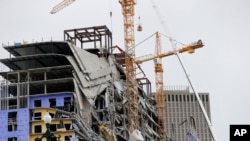 Workers in a bucket hoisted by a crane begin preparing the two unstable cranes for implosion at the Hard Rock Hotel, which partially collapsed while under construction, Oct. 12, 2019, in New Orleans.