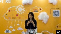 FILE - A woman uses her smartphone near a booth promoting cloud services during the Global Mobile Internet Conference in Beijing, China.