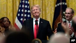 President Donald Trump, standing with LaSonya Hill, left, and Guy Berkebile, right, speaks about taxes during an event in the East Room of the White House in Washington, June 29, 2018. 