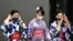 Women in traditional costumes, wearing protective face masks, walk outside the National Stadium, the main venue of the Tokyo 2020 Olympic Games, in Tokyo, Japan, Aug. 3, 2021.