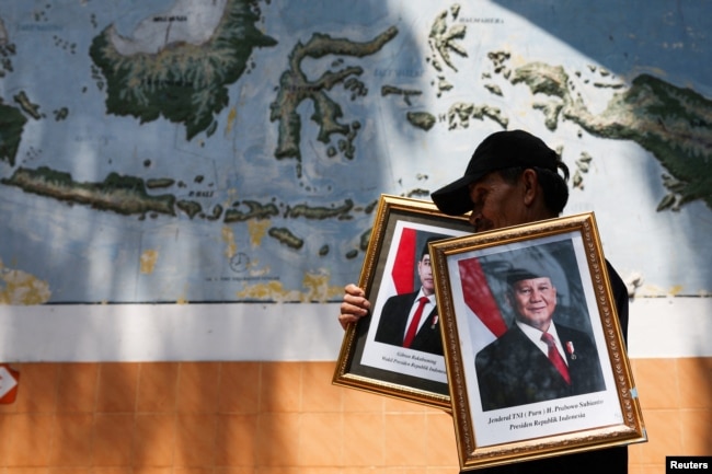 Seorang pekerja membawa potret Presiden baru Indonesia Prabowo Subianto dan Wakil Presiden baru Gibran Rakabuming Raka di SD Pondok Labu 14 Pagi, di Jakarta, 22 Oktober 2024. (Ajeng Dinar Ulfiana/REUTERS)