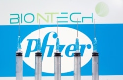 FILE - Syringes are seen in front of displayed Biontech and Pfizer logos in this illustration taken November 10, 2020.