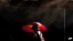 FILE - A woman protects herself from the sun with an umbrella as she passes a water mist machine to cool down during a hot day at Ledras pedestrian shopping street in the capital Nicosia, Cyprus, July 26, 2023.