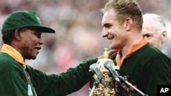 FILE - Nelson Mandela, himself wearing a Springbok rugby jersey, presents the World Cup trophy to South Africa team captain, Francois Pienaar, at Johannesburg’s Ellis Park Stadium in 1995.