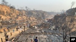 Rohingya refugees look at the remains of Monday's fire at the Rohingya refugee camp in Balukhali, southern Bangladesh that destroyed hundreds of shelters and left thousands homeless, March 23, 2021. 